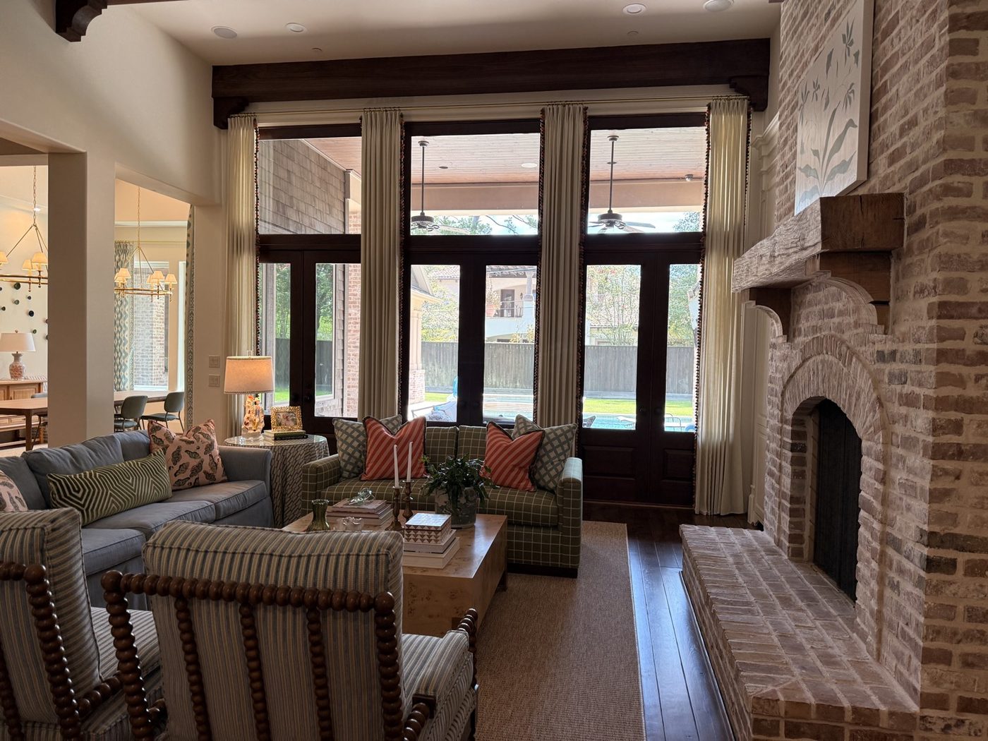 Cream drapery with trim on tall glass doors beside a brick fireplace