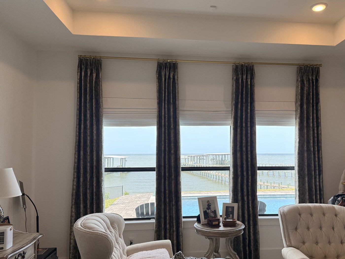 Textured drapery panels and Roman shades on a wide window over the water